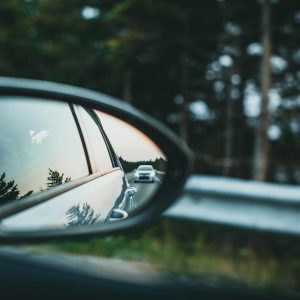 A car is reflected in a side mirror on a scenic forest road.